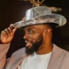 Man tipping a silver mirror disco cowboy hat, wearing a beige blazer