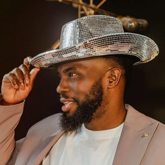 Man tipping a silver mirror disco cowboy hat, wearing a beige blazer