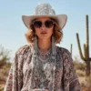 Woman styling a disco cowboy hat with sunglasses and layered silver jewelry in the desert